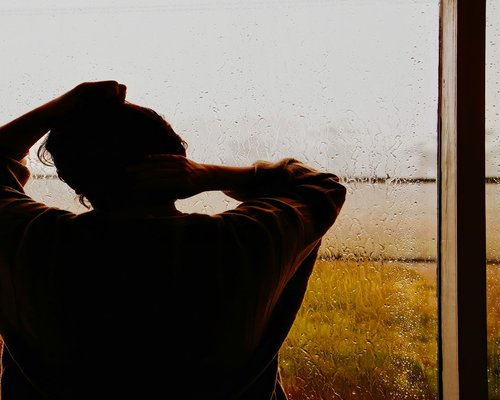 Person relaxing, holding a glass of water looking out the window